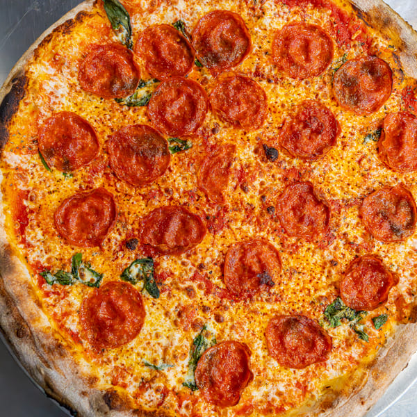 A freshly baked pepperoni pizza with melted cheese and basil on a metal surface.