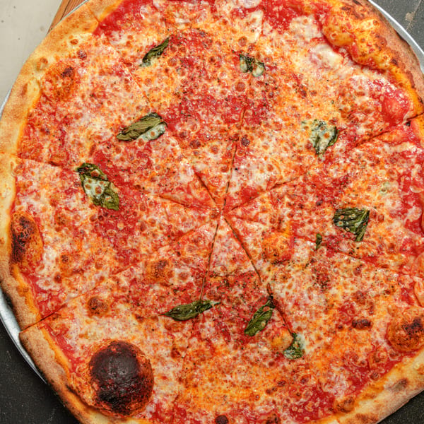 A large, sliced Margherita pizza with melted cheese, red sauce, and basil leaves on a dark surface.