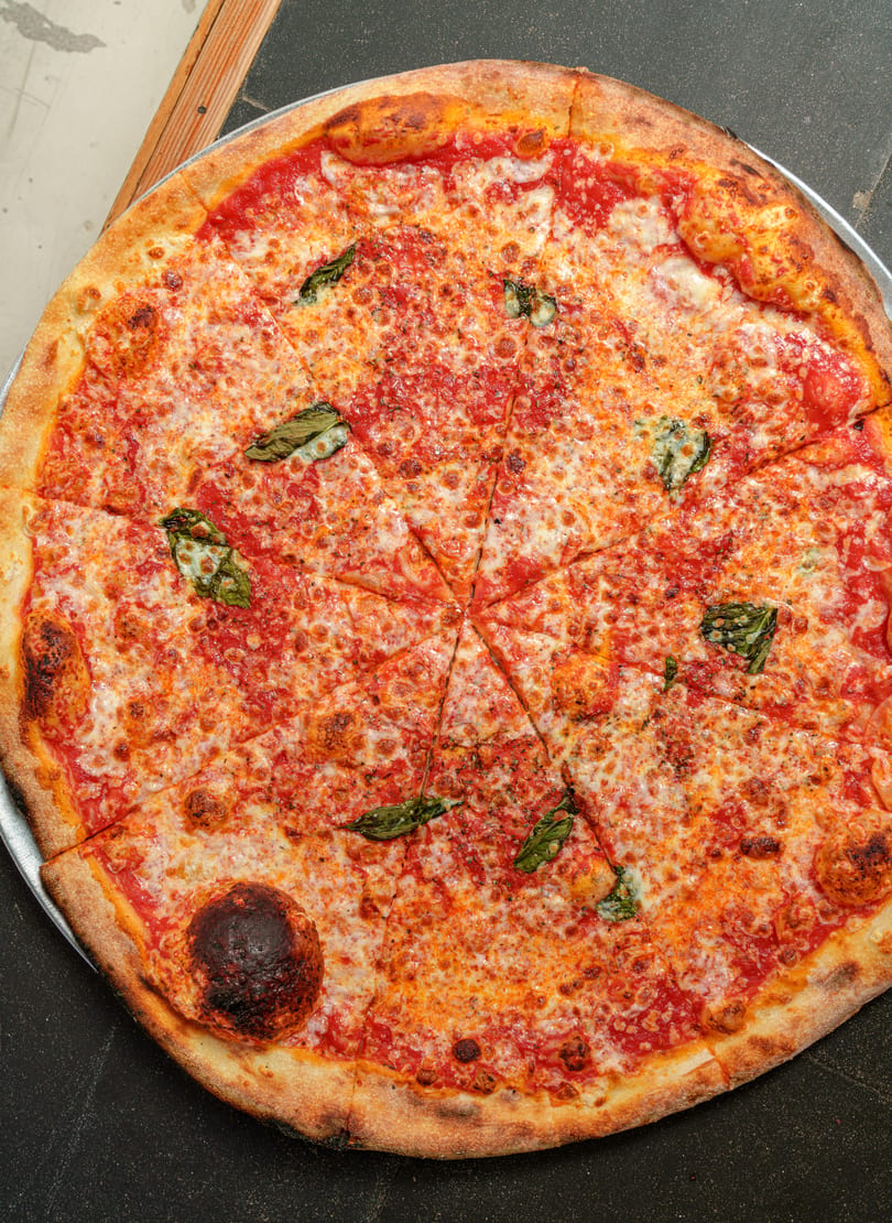 Overhead view of a whole, sliced Margherita pizza with basil leaves on a metal tray.