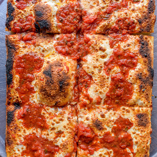 A square Detroit-style pizza with crispy charred edges, topped with melted cheese and dollops of red sauce.