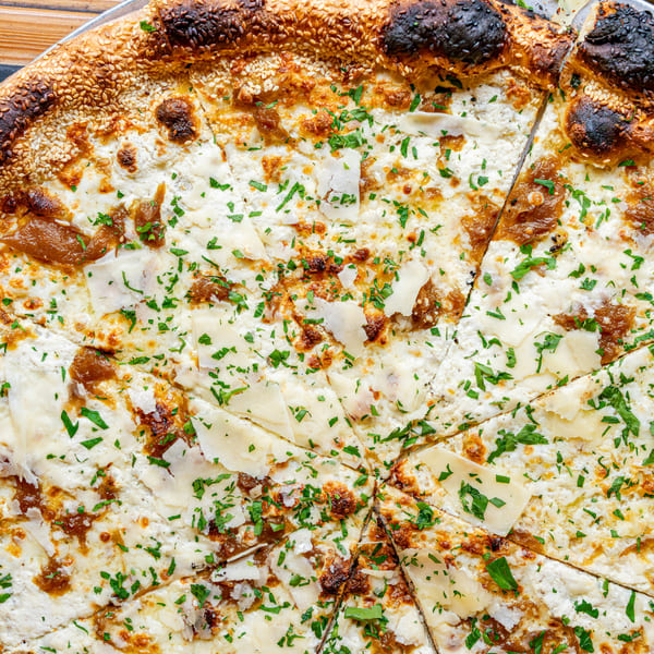 Close-up of a white pizza with caramelized onions, parmesan, and parsley, sliced on a metal tray.