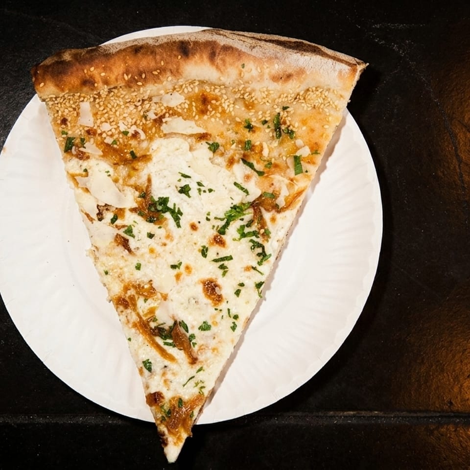 A slice of white pizza with caramelized onions, cheese, and parsley on a white paper plate.